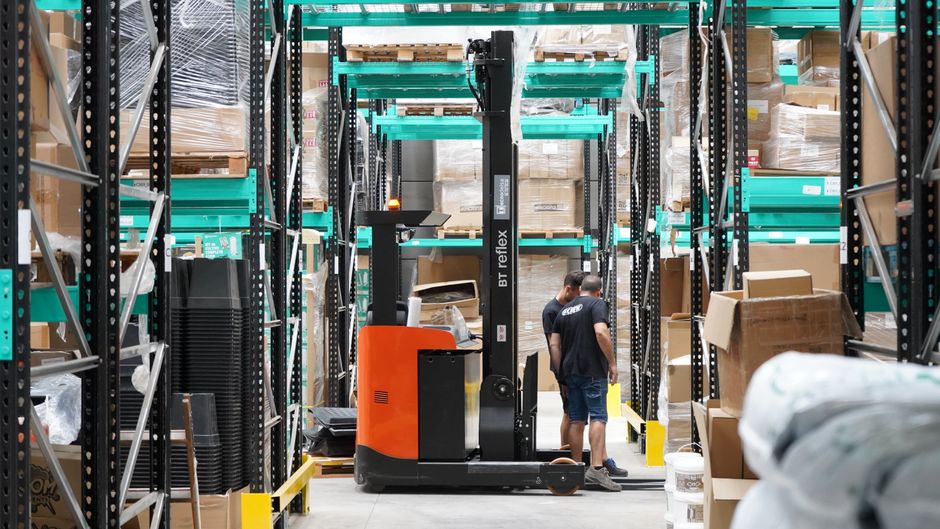 Warehouse scene featuring workers and a forklift navigating aisles for logistics and inventory management.
